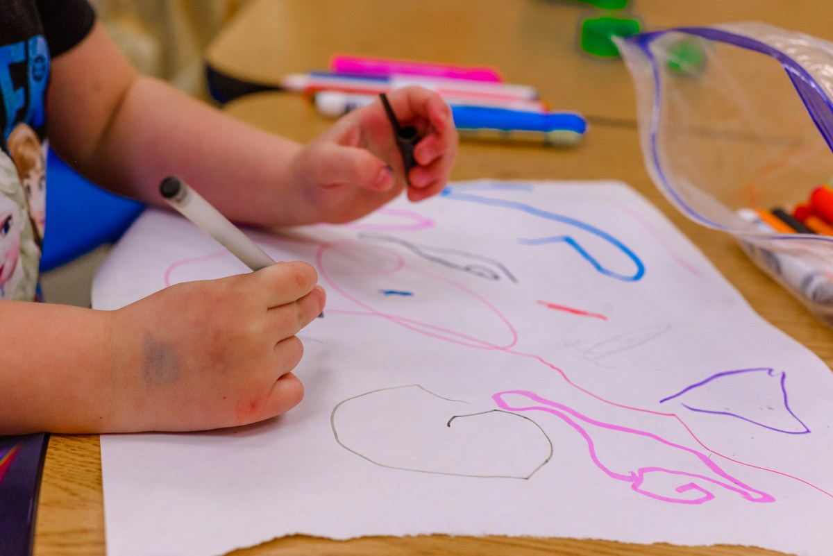 A child draws colourful looping shapes on white paper with a marker. Illustrative photo for this preview activity.