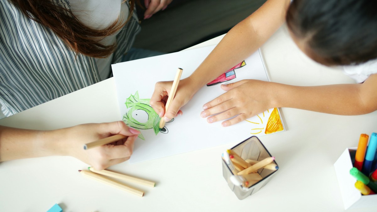 An adult and child colour a picture together with pencils at a white table. Illustrative photo for this preview activity.