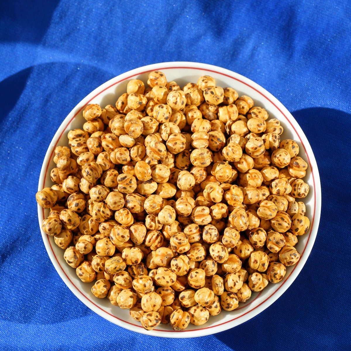 A white bowl of roasted chickpeas on a blue cloth. Illustrative food photograph; the finished recipe may look different.