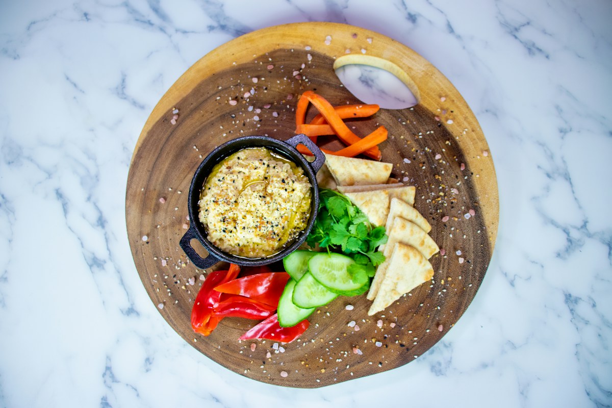 Hummus surrounded by fresh vegetables and bread. Illustrative food photograph; the finished recipe may look different.