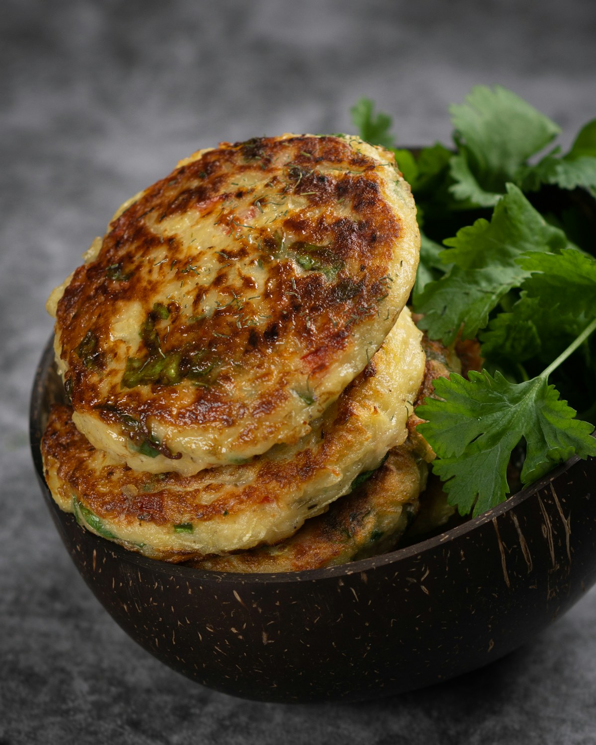 Golden courgette and potato fritters on a dark plate. Illustrative food photograph; the finished recipe may look different.