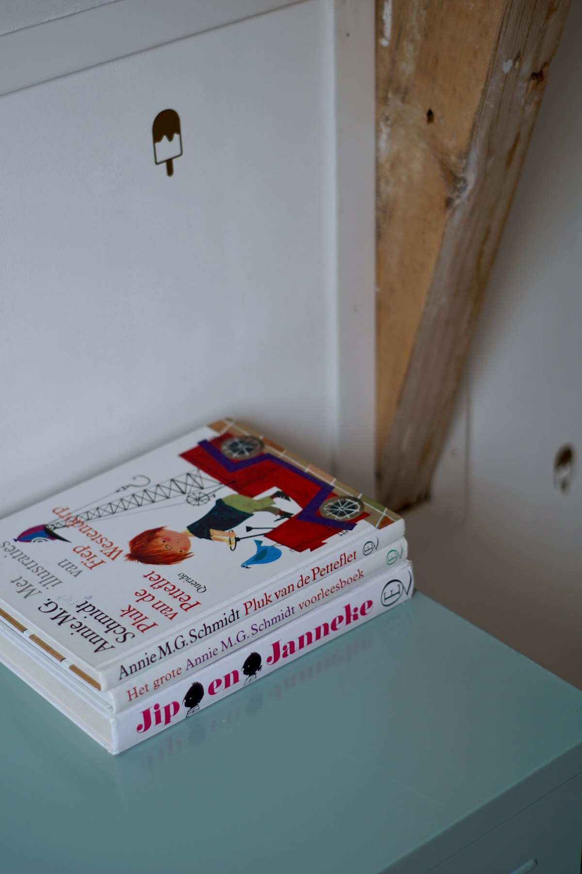 Three illustrated children's books stacked on a pale blue table. Illustrative photograph for an original fictional story.