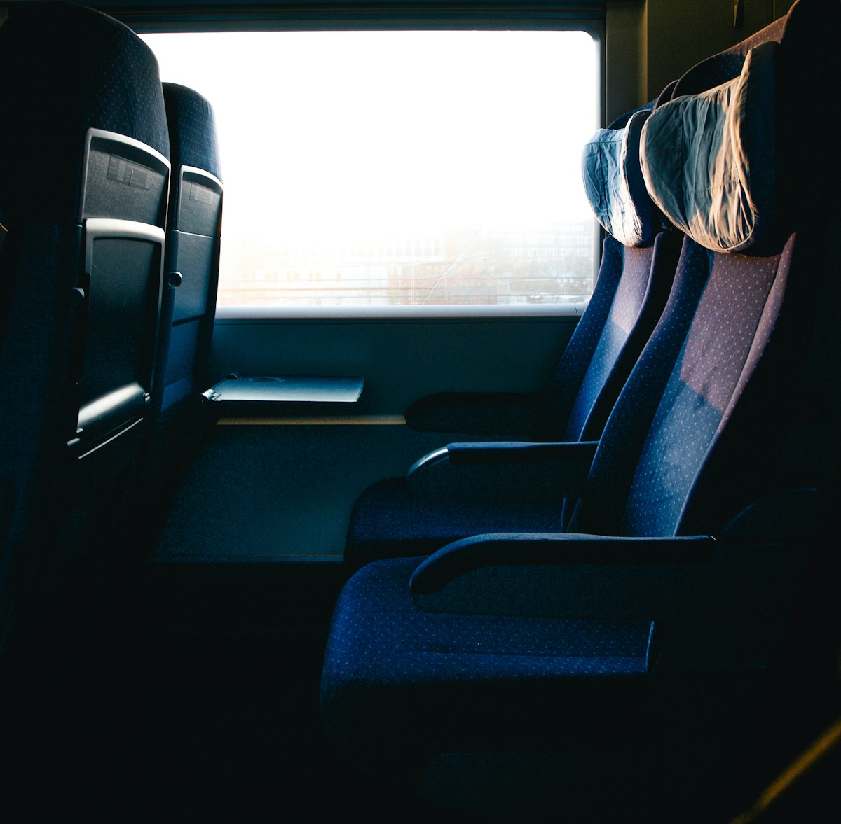 Empty blue train seats beside a sunlit window. Illustrative photograph for an original fictional story.