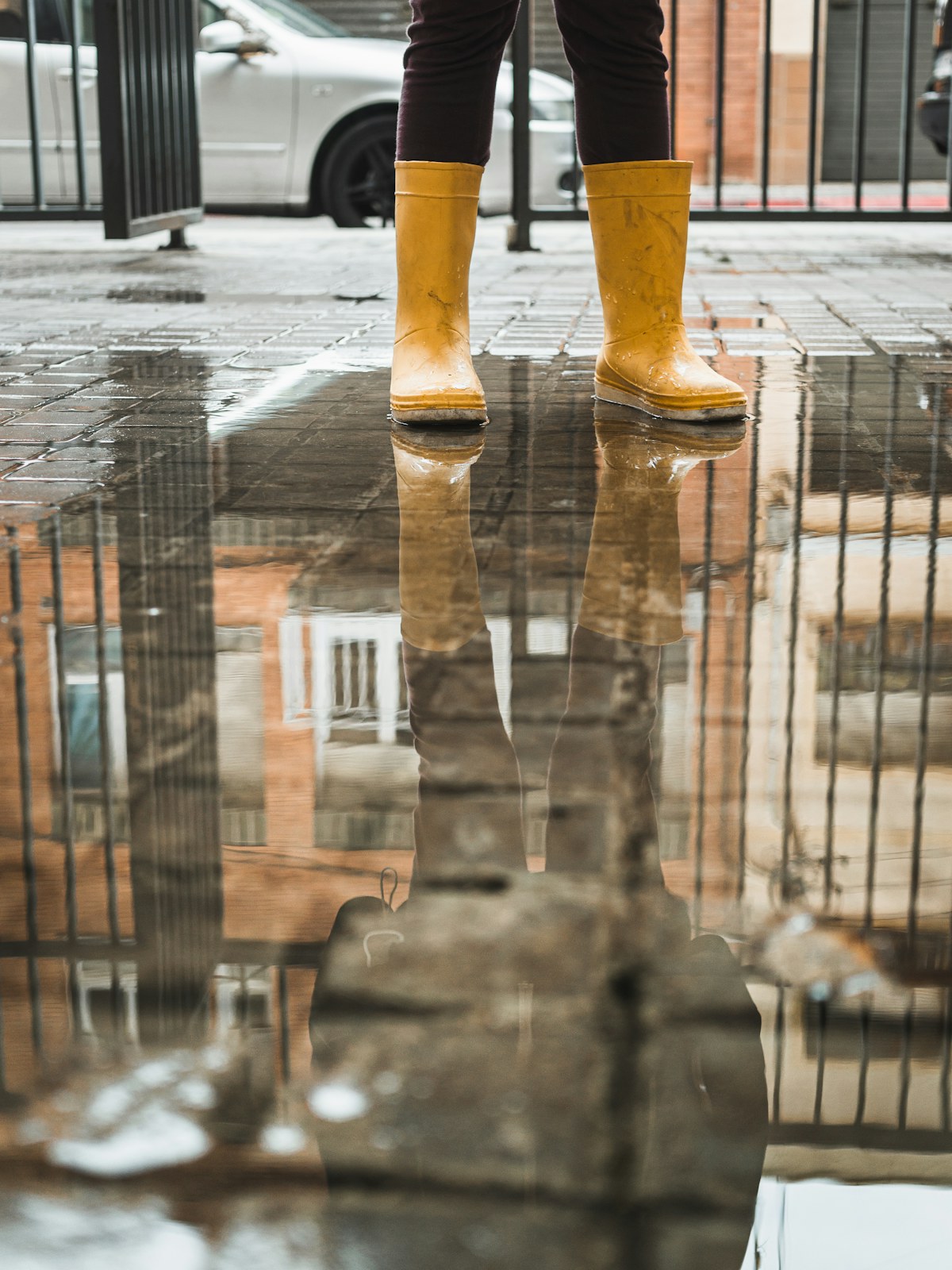 Yellow rain boots reflected in a puddle on the pavement. Illustrative photograph for an original fictional story.